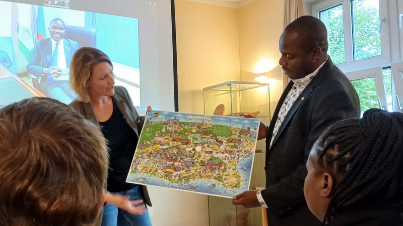 Lieselotte Heinz überreichte Donald Mwanza und Angela Kampinda das Dormagener Wimmelbild, im Hintergrund Bürgermeister George Mwanza 